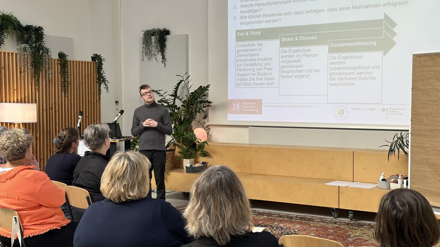 Ein Mann steht am Rednerpult vor einer Präsentation und spricht zum Publikum.