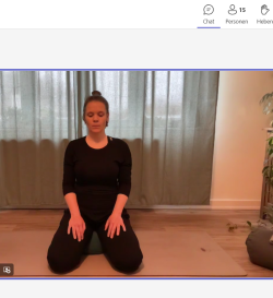 Eine junge Yoga-Lehrerin zeigt eine Entspannungsübung und einige Teilnehmende machen mit.