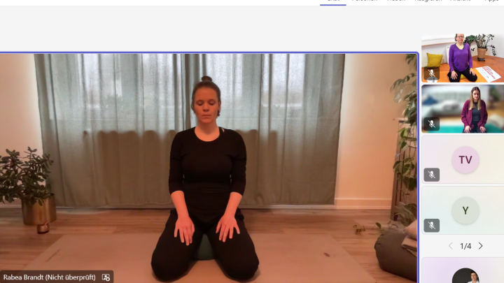 Eine junge Yoga-Lehrerin zeigt eine Entspannungsübung und einige Teilnehmende machen mit.