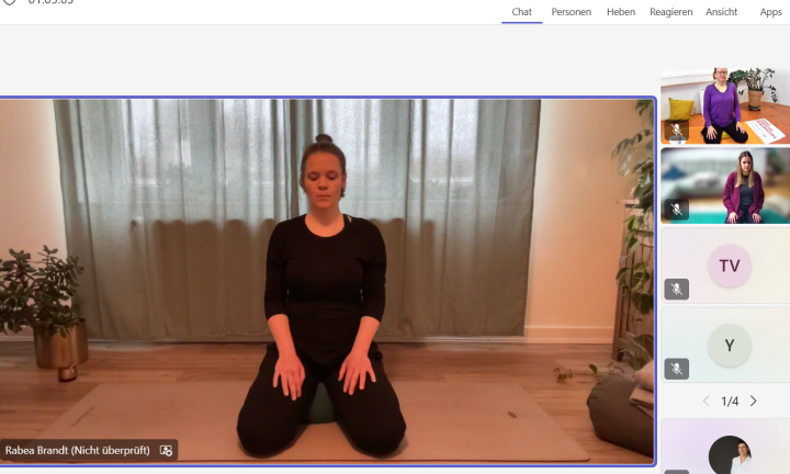 Eine junge Yoga-Lehrerin zeigt eine Entspannungsübung und einige Teilnehmende machen mit.